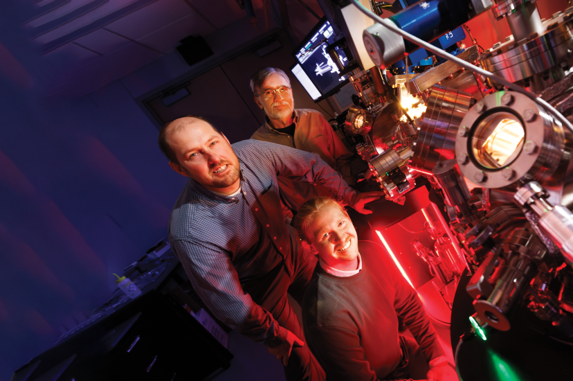 Craig Zuhlke (left), George Gogos (back) and doctoral student Graham Kaufman (front), pose with a Leybold ultra-high vacuum laser surface processing and materials analysis system