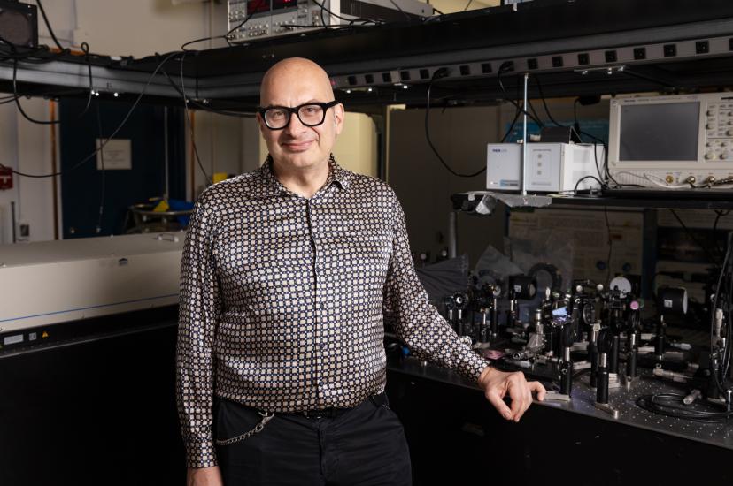 A bald man with glasses stands at an electronics bench