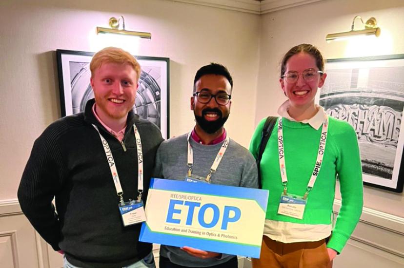 A fair-haired man, a dark-haired man with a beard and glasses, and a woman with light brown hair and glasses, hold a sign in a hotel corridor that says ETOP in blue letters
