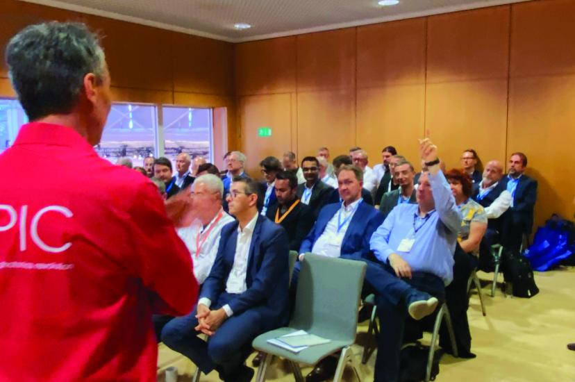 A man in a red shirt that says EPIC stands with his back to the camera in front of a conference room 