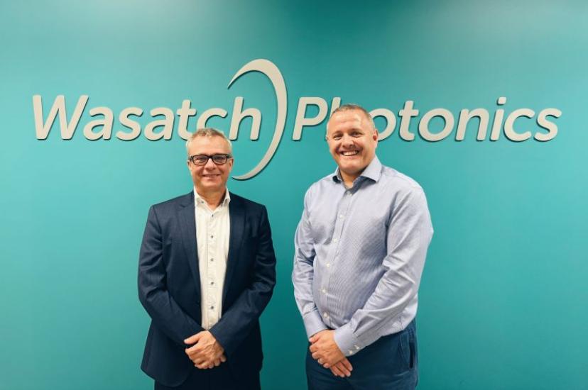 Two white men stand in front of a green wall. The words on the wll read Wasatch Photonics