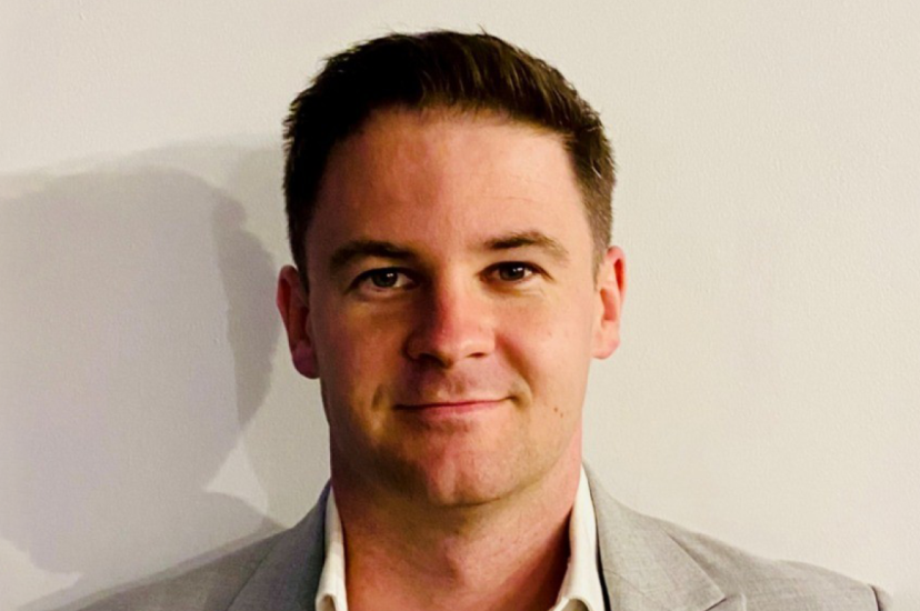 A white man with brown hair, wearing a beaige suit