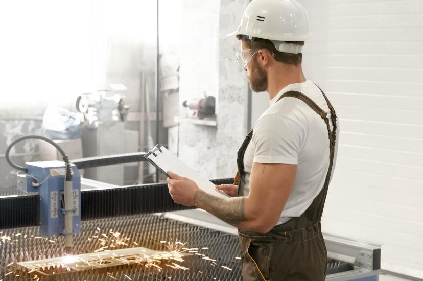 Man with safety glasses and helmet working with laser cutter