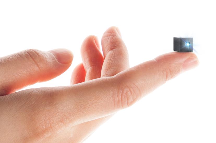 A human hand, on which an outstretched finger holds a tiny black cube