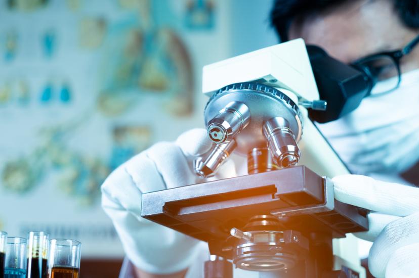 Doctor or scientist wearing medical face mask and looking in microscope while working on medical research in science laboratory