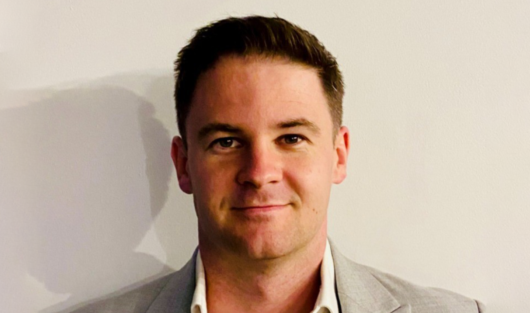 A white man with brown hair, wearing a beaige suit