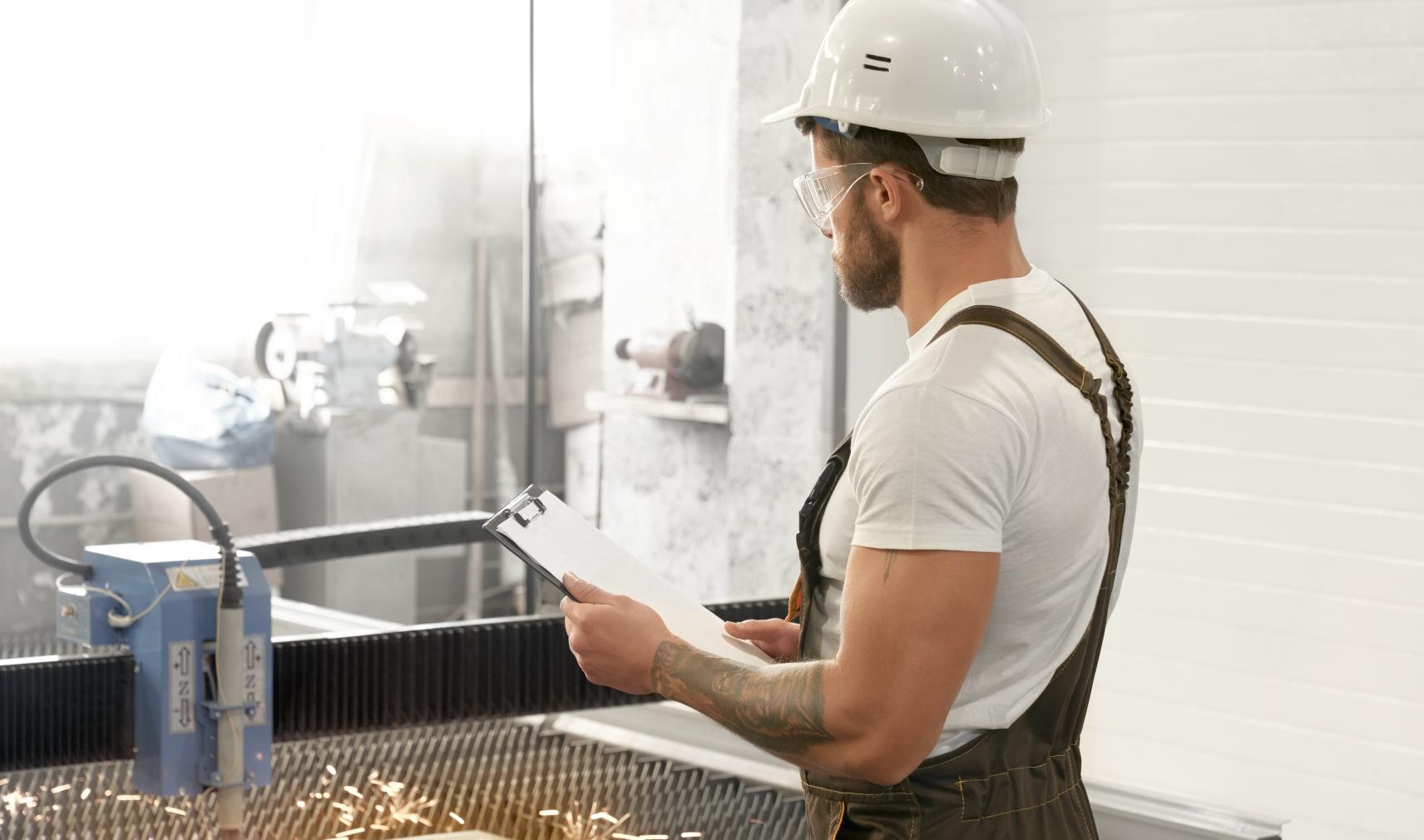 Man with safety glasses and helmet working with laser cutter