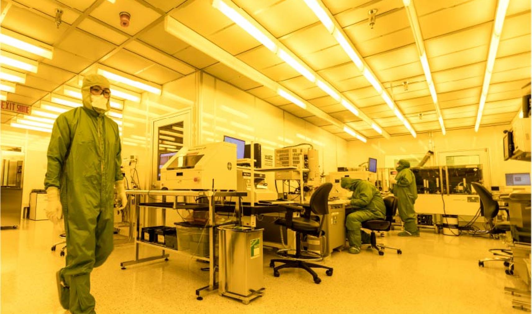 Technician in full PPE walks across a lab at the Canadian Photonics Fabrication Centre