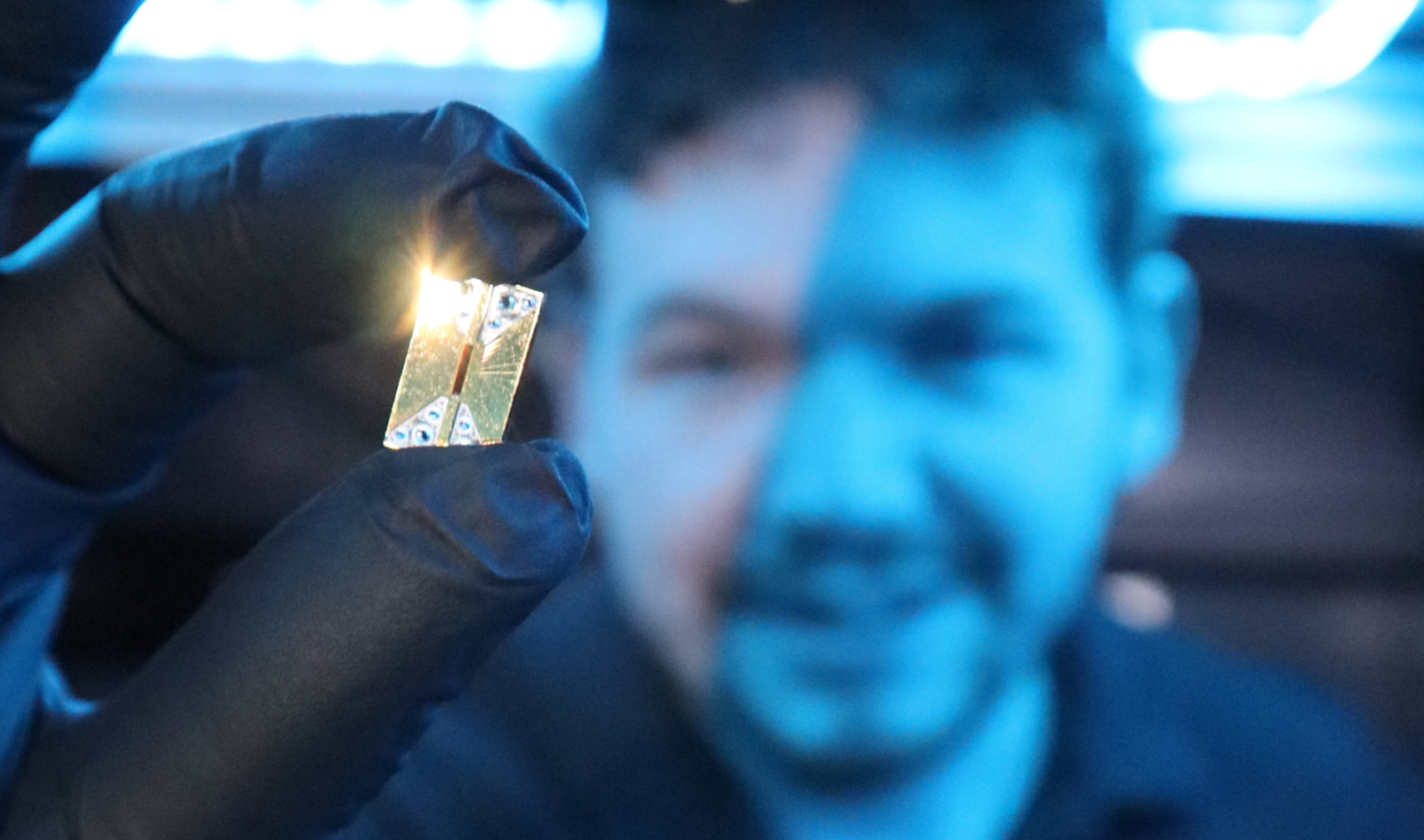 Main holds Photonic integrated circuit chip in the foreground of an image