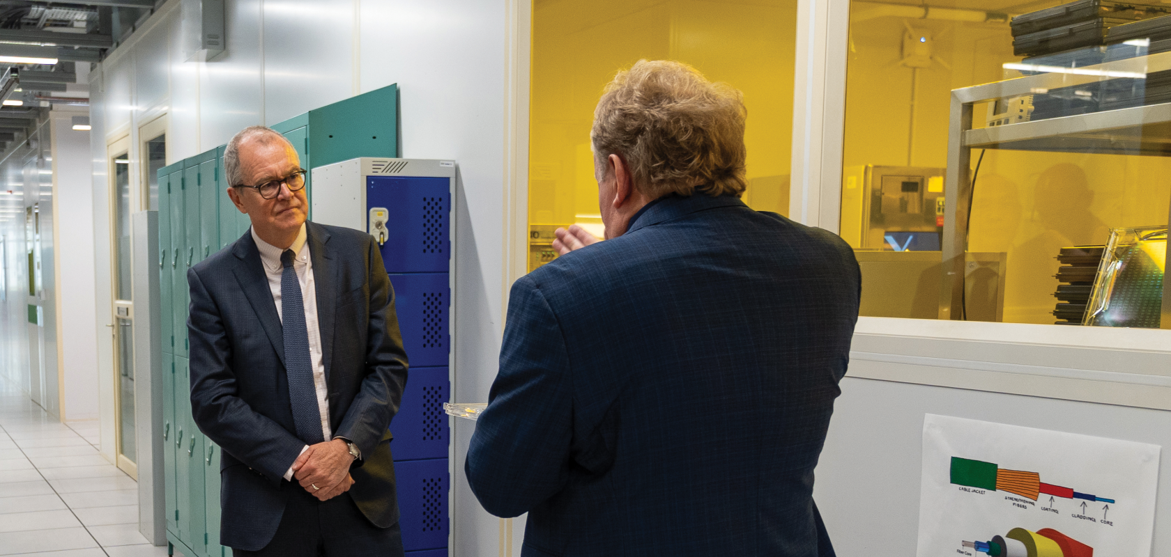Two men in dark suits, one with his back to the camera, stand in the corridor of Southmpton University's Optoelectronics Research Centre