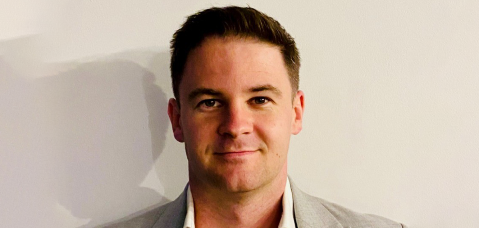 A white man with brown hair, wearing a beaige suit