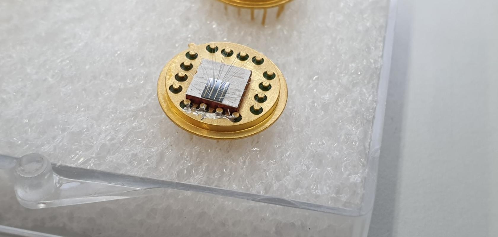 A golden optical modulator chip on a white background