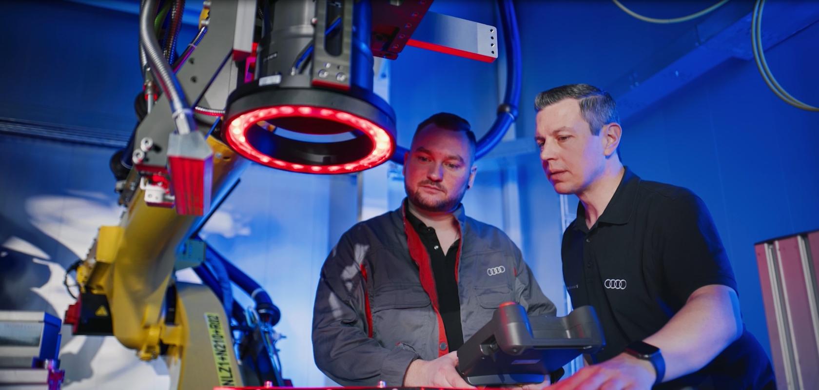 Two men stand behind a large robot arm containing a laser and imaging equipment