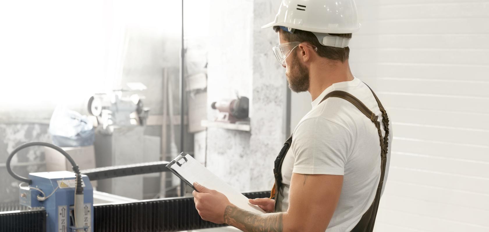 Man with safety glasses and helmet working with laser cutter