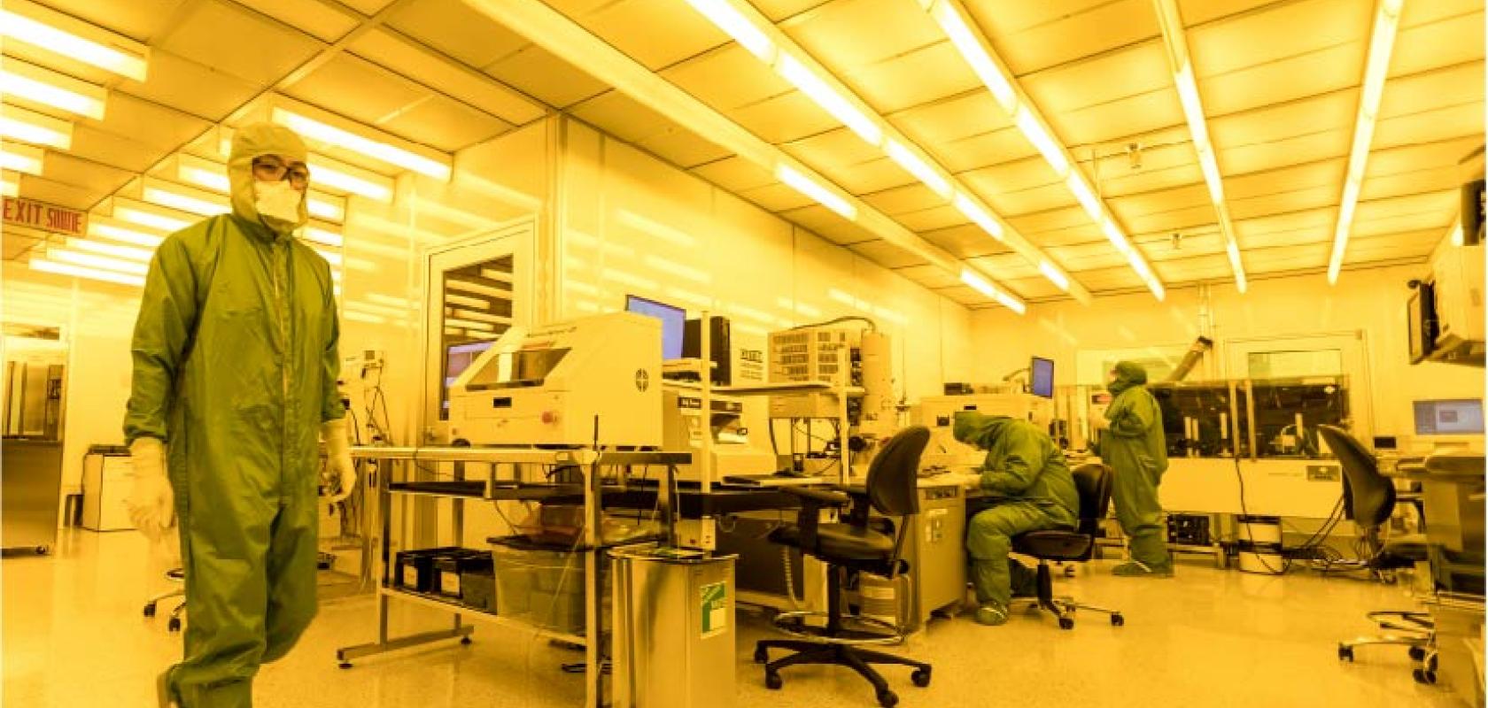 Technician in full PPE walks across a lab at the Canadian Photonics Fabrication Centre
