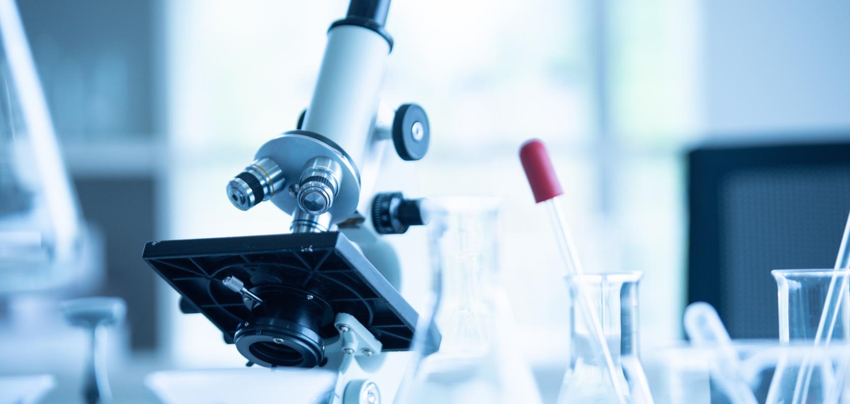 A stock image of a laboratory microscope surrounded by test tubes