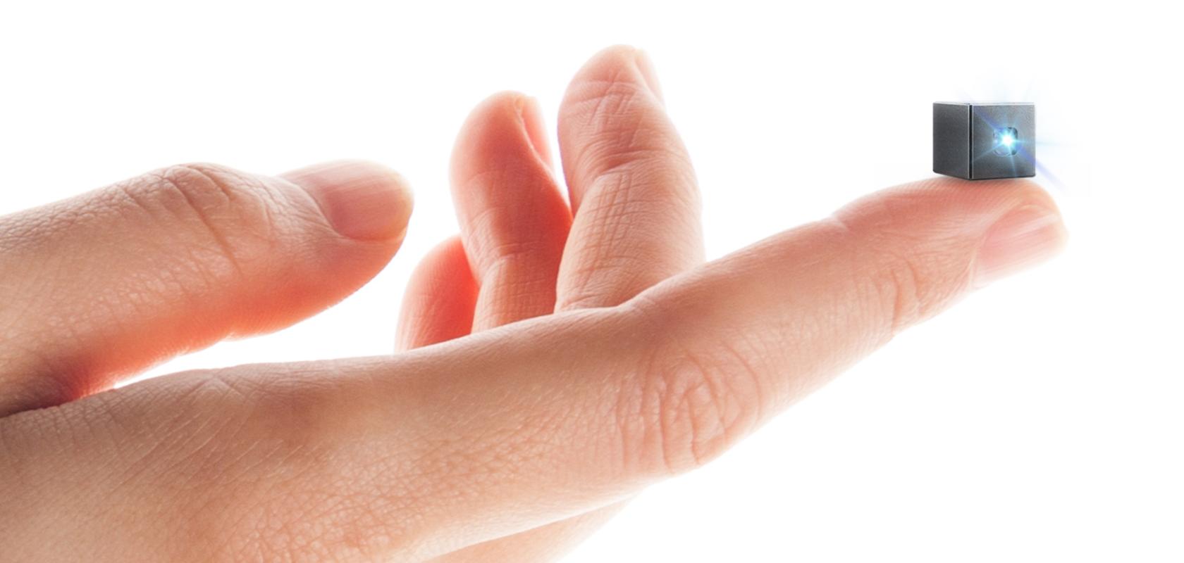 A human hand, on which an outstretched finger holds a tiny black cube