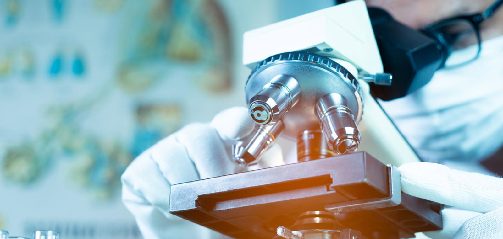 Doctor or scientist wearing medical face mask and looking in microscope while working on medical research in science laboratory