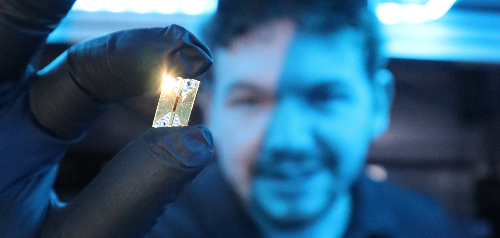 Main holds Photonic integrated circuit chip in the foreground of an image