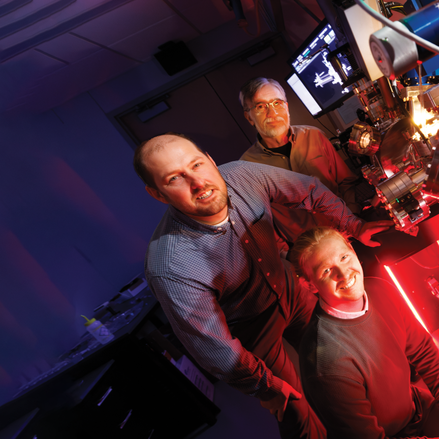 Craig Zuhlke (left), George Gogos (back) and doctoral student Graham Kaufman (front), pose with a Leybold ultra-high vacuum laser surface processing and materials analysis system