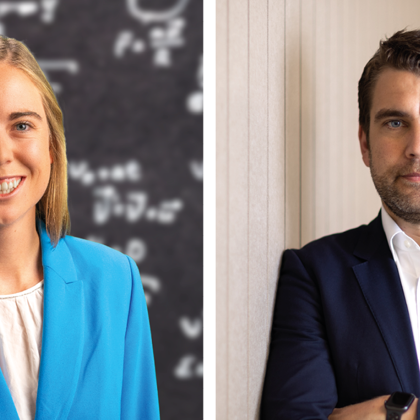 A woman with blonde hair weairng a blue suit stands in front of a blackboard of equations on the left, and right, a dark-haired man wearing a suit stands, arms folded, in front of a beige background