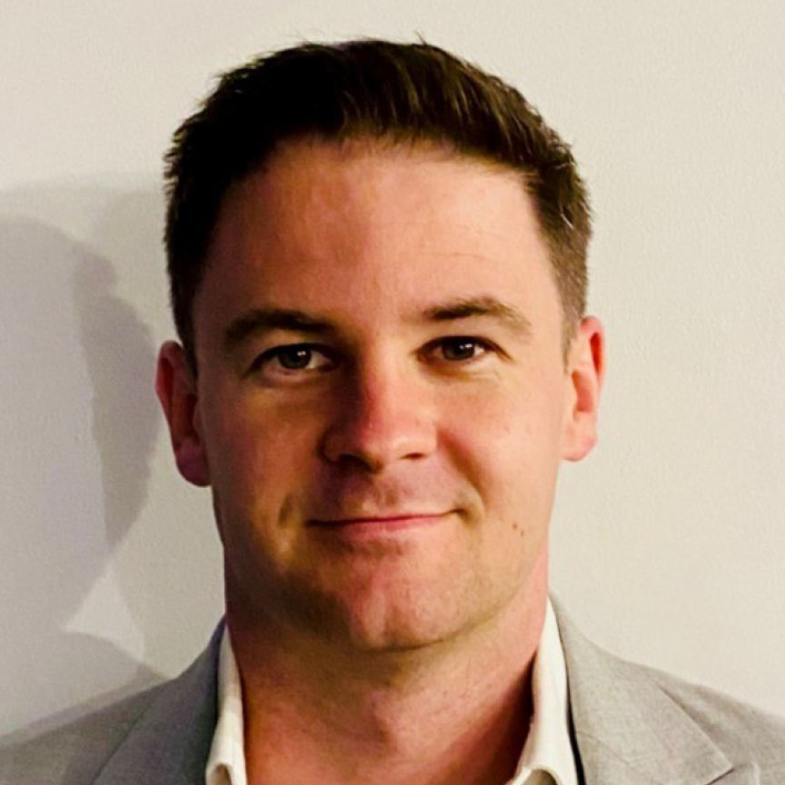 A white man with brown hair, wearing a beaige suit