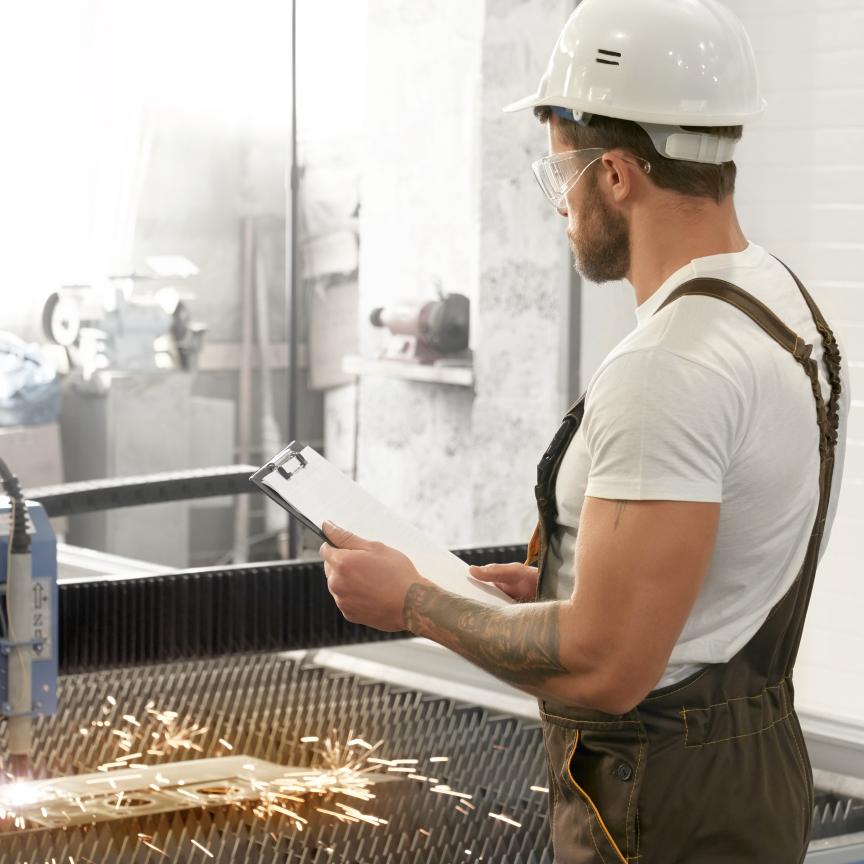 Man with safety glasses and helmet working with laser cutter
