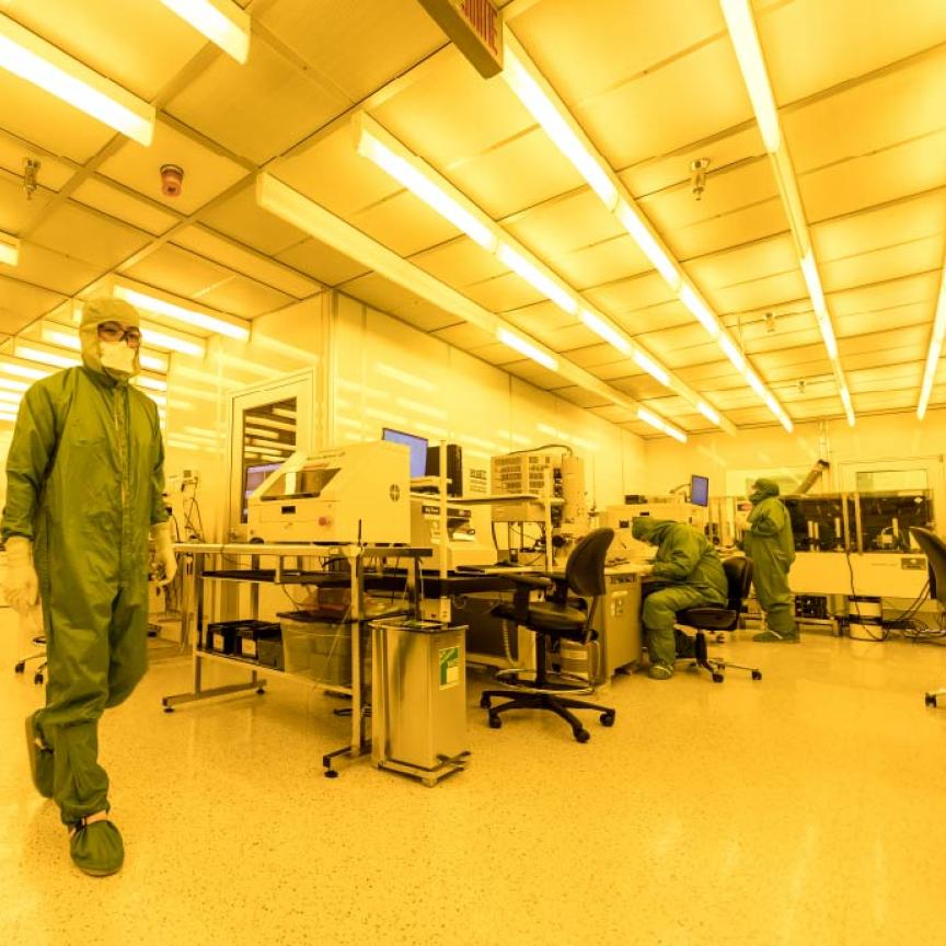 Technician in full PPE walks across a lab at the Canadian Photonics Fabrication Centre