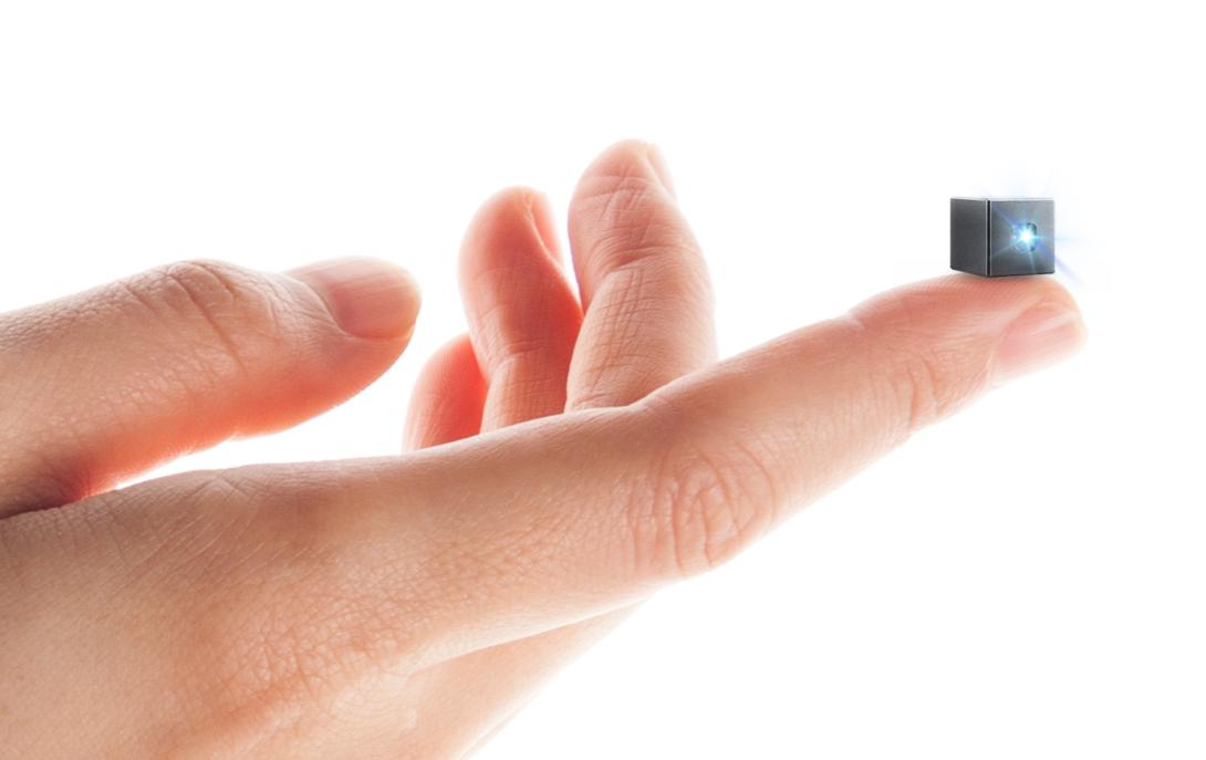 A human hand, on which an outstretched finger holds a tiny black cube